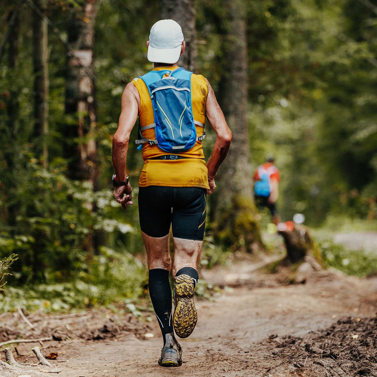 Mężczyzna biegnący po leśnej ścieżce z plecakiem i w odzieży sportowej. - tytułowa