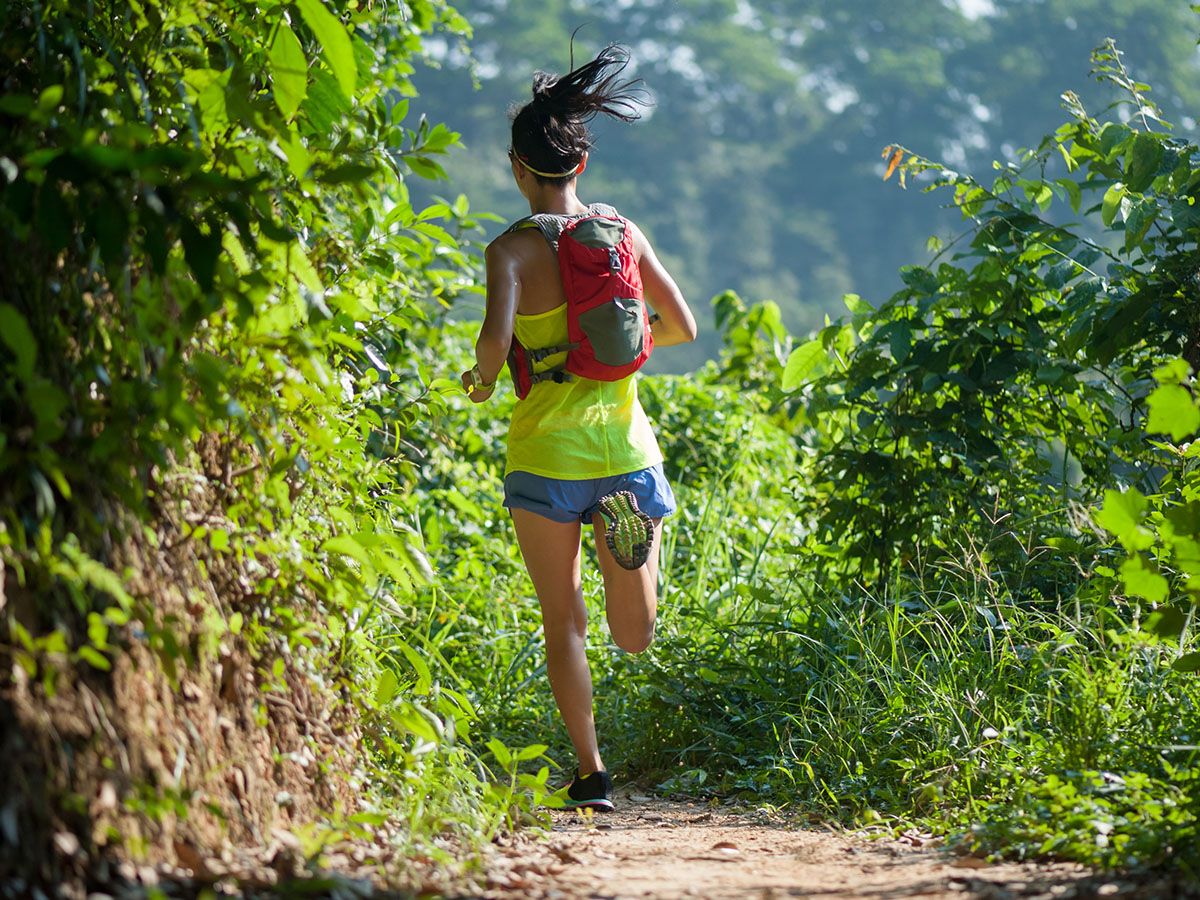 Kobieta biegnąca w słonecznym terenie, ubrana w sportowy strój i plecak. - zdjęcie