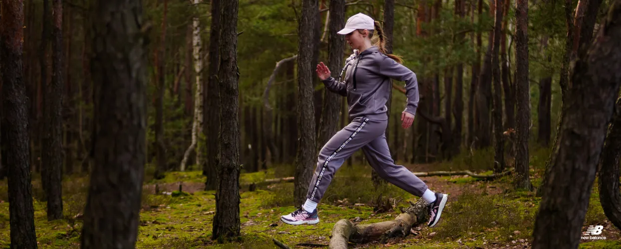 Egy sportruhás és cipős nő fut az erdőben.