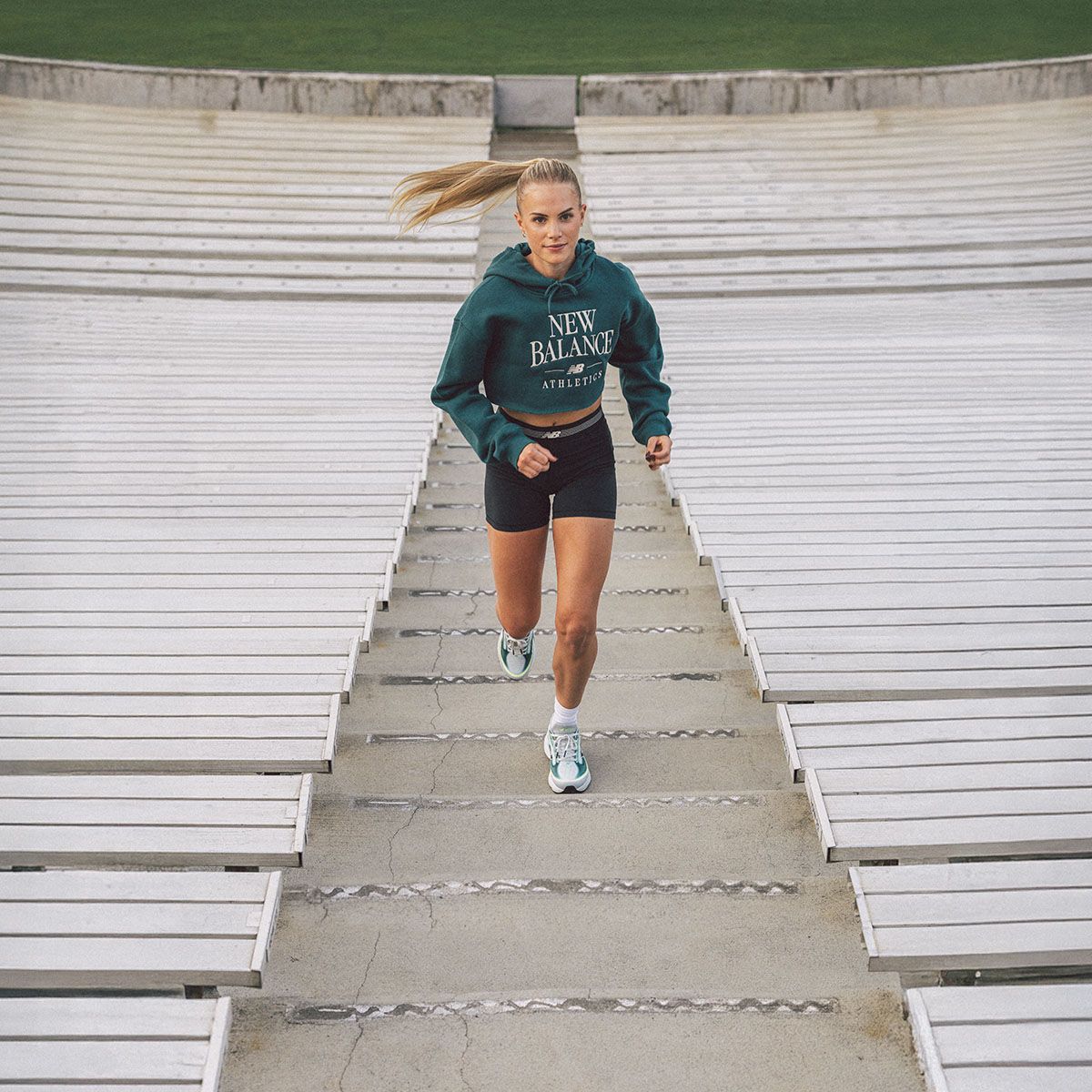 Kobieta biegnie po schodach stadionu w sportowym stroju i butach New Balance. - tytułowa